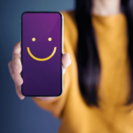 woman with yellow sweater holding up mobile phone with smiley face: how barcode labels improve customer service