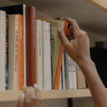 A person pulling out a book from a library collection after understanding the significance of an ISBN.