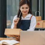 A woman checking her laptop while preparing shipment boxes for selling on Amazon with GS1 barcodes.