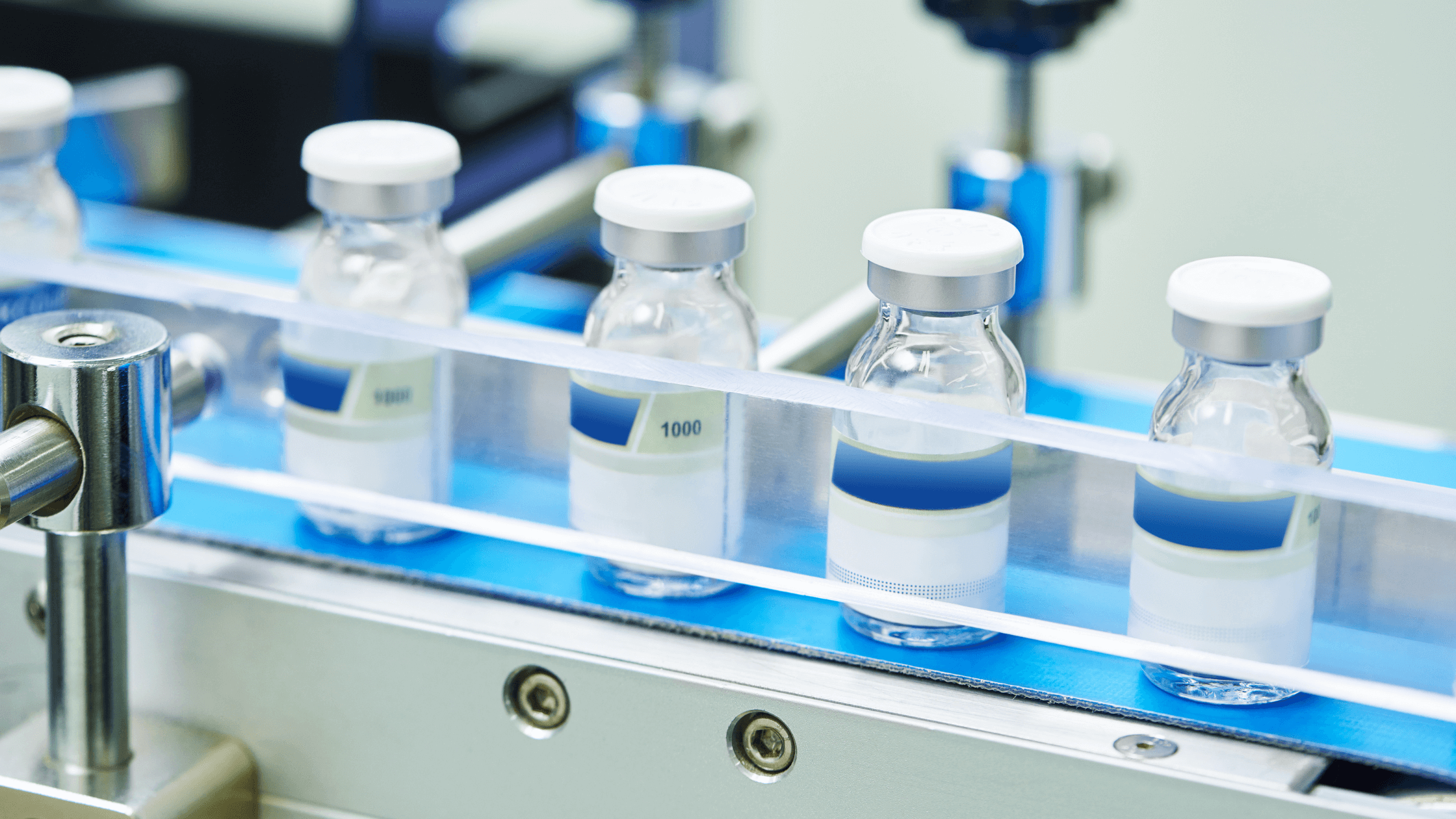 Glass vials with white caps move along a blue conveyor belt in preparation to adhere to pharmaceutical barcode standards